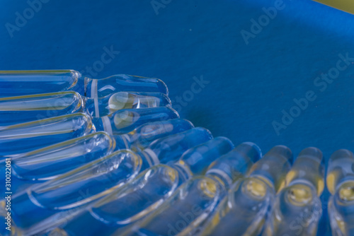 Glass medical ampoule vial for injection. Medicine is liquid sodium chloride with of aqueous solution in ampulla. Close up. Bottles ampule multicolor on background color and water. Human plasma.