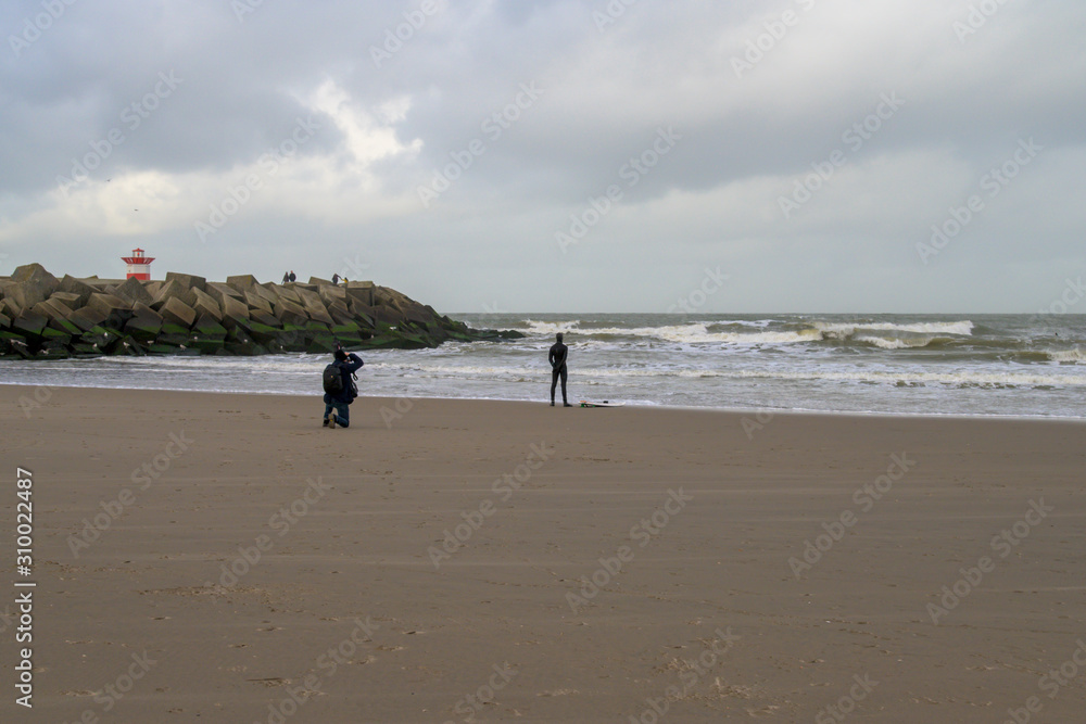 Photographer on the beach of Scheveningen photographing a man in wetsuit looking out over the sea.