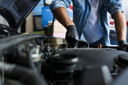 Man in shirt and gloves working in car repair service and fixing car engine