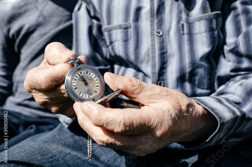 Old man's hands holding silver pocket clock, close-up photo