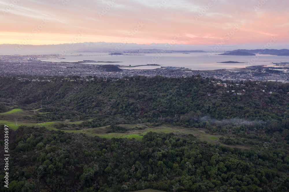 A serene sunset illuminates the densely populated San Francisco Bay area including Oakland, Berkeley, Emeryville, El Cerrito, and San Francisco in the distance.