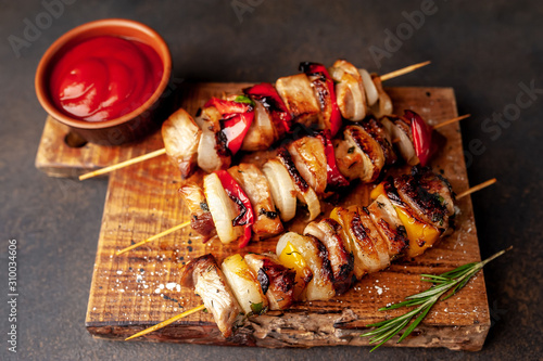 Skewers of meat with grilled vegetables on a cutting board on a stone background