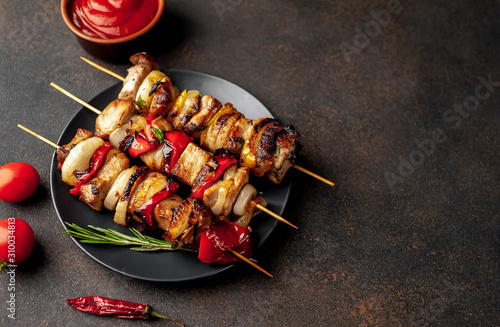 Meat skewers with grilled vegetables on a black plate on a stone background with copy space for your text