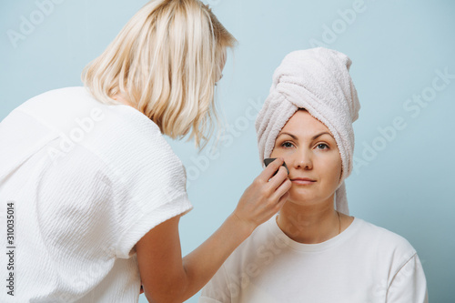 Female hairdresser applying setting powder on client's cheeks over blue.