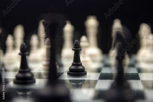 black pawn close-up on a background of white pieces on a chessboard