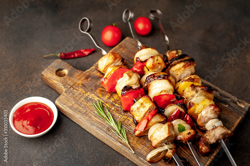 Skewers of meat with grilled vegetables on a cutting board on a stone background