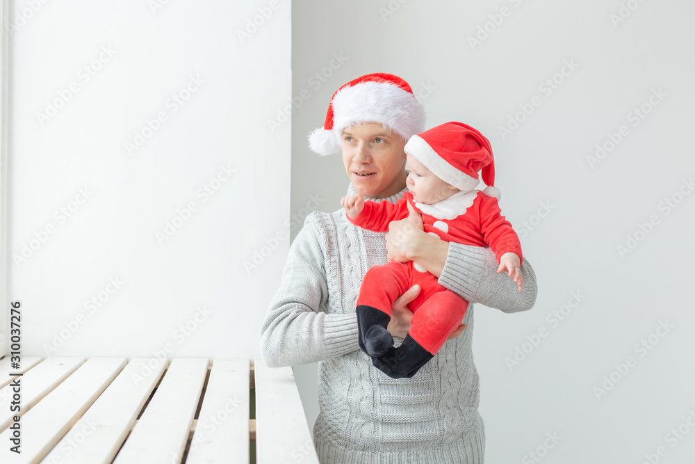 Obraz premium Fatherhood and holidays concept - Father with his baby boy wearing Santa hats celebrating Christmas