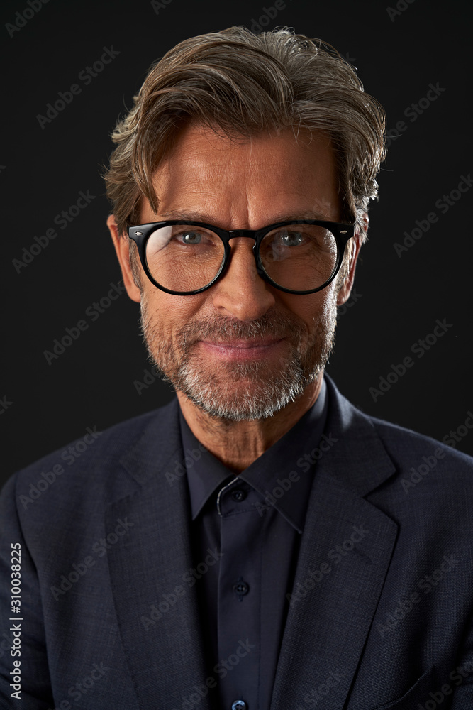 Portrait of smiling mature businessman wearing glasses against dark background Portrait of smiling mature businessman wearing glasses against dark background