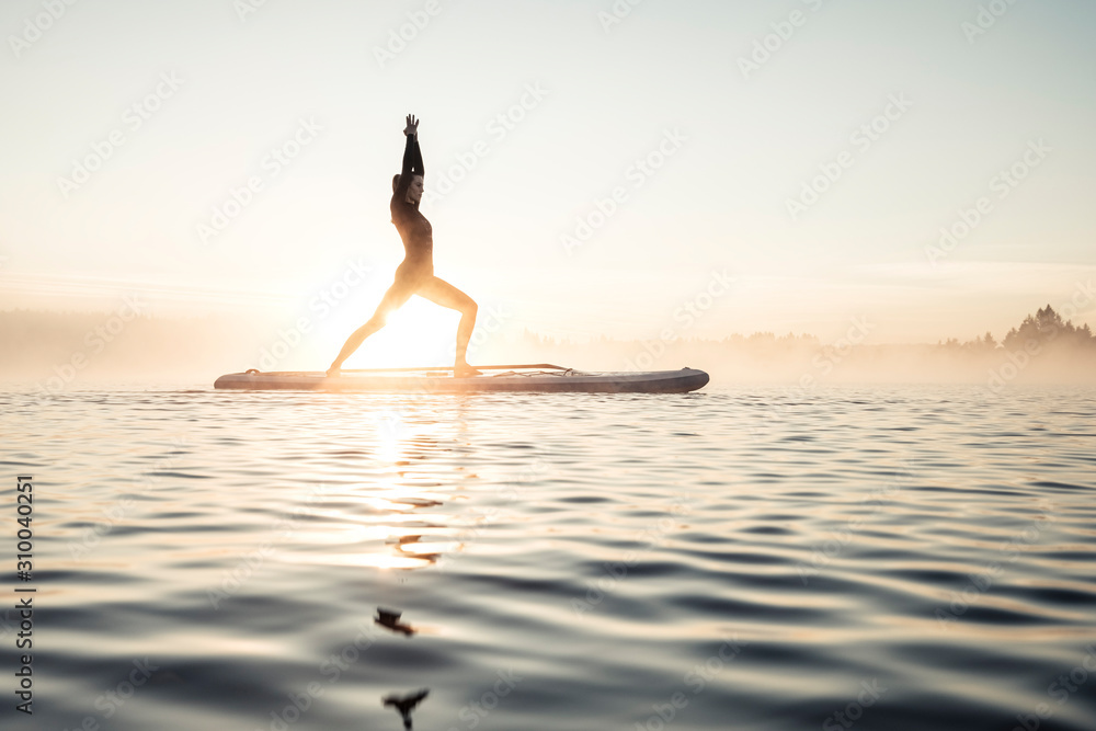 Woman practicing paddle board yoga on lake Kirchsee in the morning, Bad Toelz, Bavaria, Germany Woman practicing paddle board yoga on lake Kirchsee in the morning, Bad Toelz, Bavaria, Germany