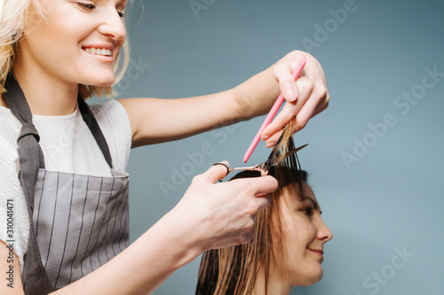 Happy blonde female barber trimming client's hair over blue background.