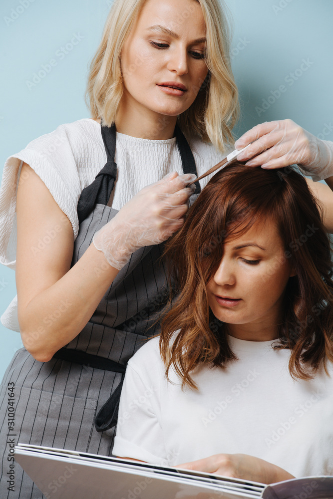 Fototapeta premium Blonde female hairdresser selecting hair tone for a client over blue background.
