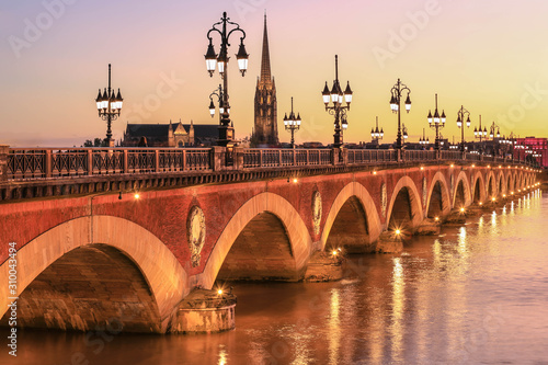 View of  Pont de Pierre bridge with St Michel churh in Bordeaux at sunset