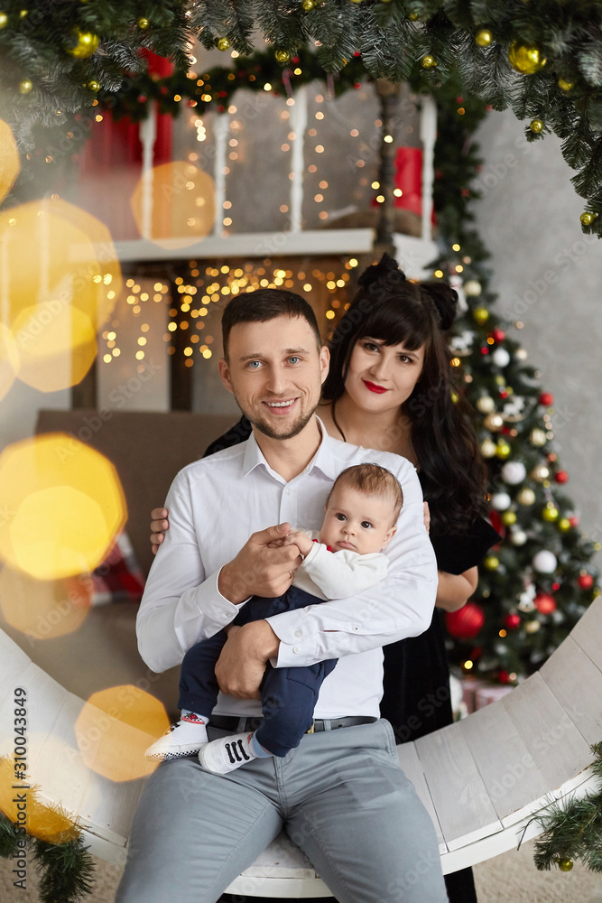 Happy family with baby in decorated for Christmas interior. Young couple with baby boy posing in decorated for New year interior. Young woman and handsome man posing with son in decorated interior Happy family with baby in decorated for Christmas interior. Young couple with baby boy posing in decorated for New year interior. Young woman and handsome man posing with son in decorated interior