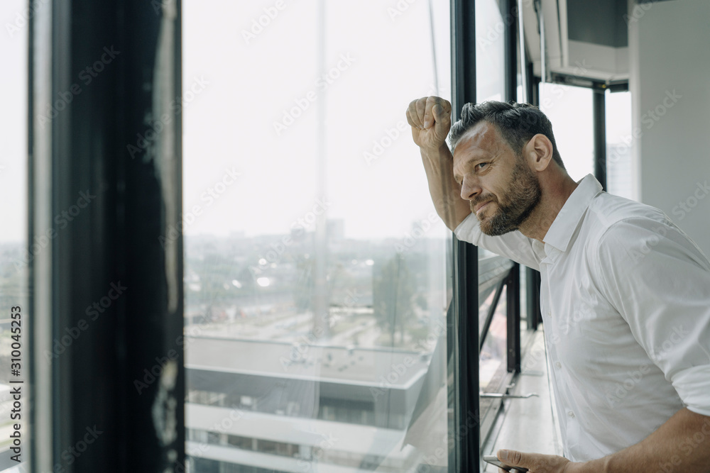 Mature businessman looking out of window in office Mature businessman looking out of window in office