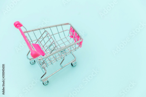 Small supermarket grocery push cart for shopping toy with wheels isolated on blue pastel colorful trendy background Copy space. Sale buy mall market shop consumer concept.