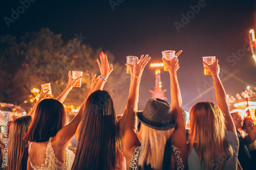 Fotografie Back view of female friends drinking beer and dancing at music festival