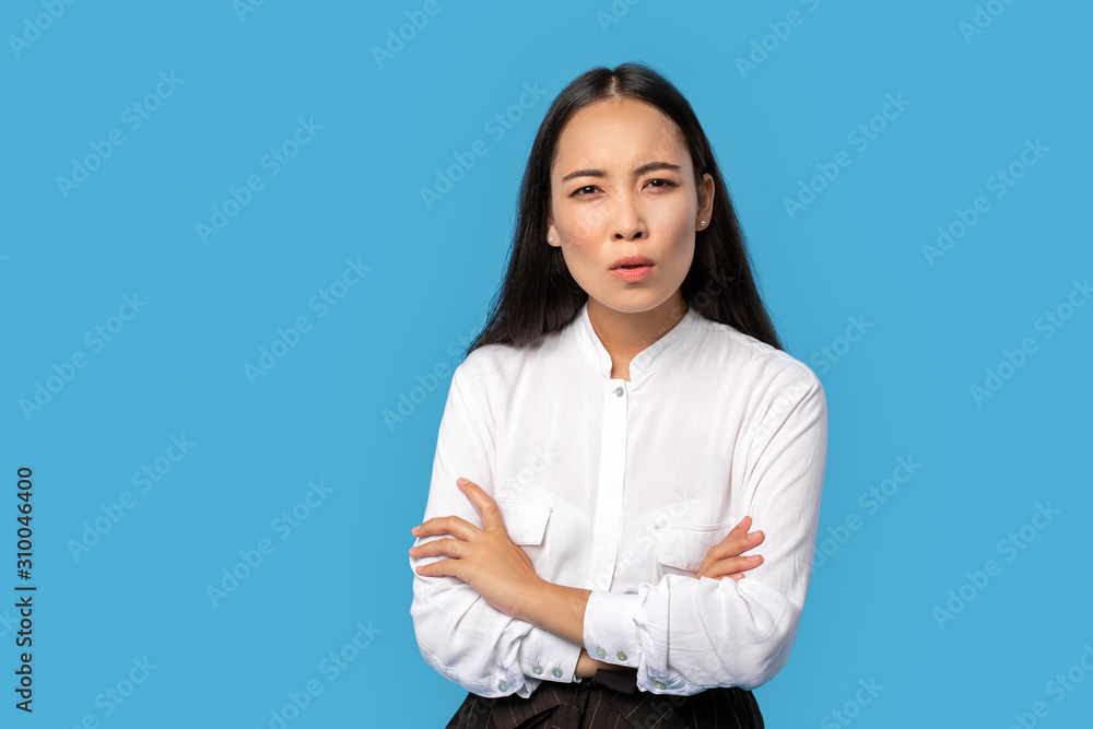 Freestyle. Young woman wearing shirt and skirt standing isolated on blue crossed arms looking camera concerned Freestyle. Young woman wearing shirt and skirt standing isolated on blue crossed arms looking camera concerned