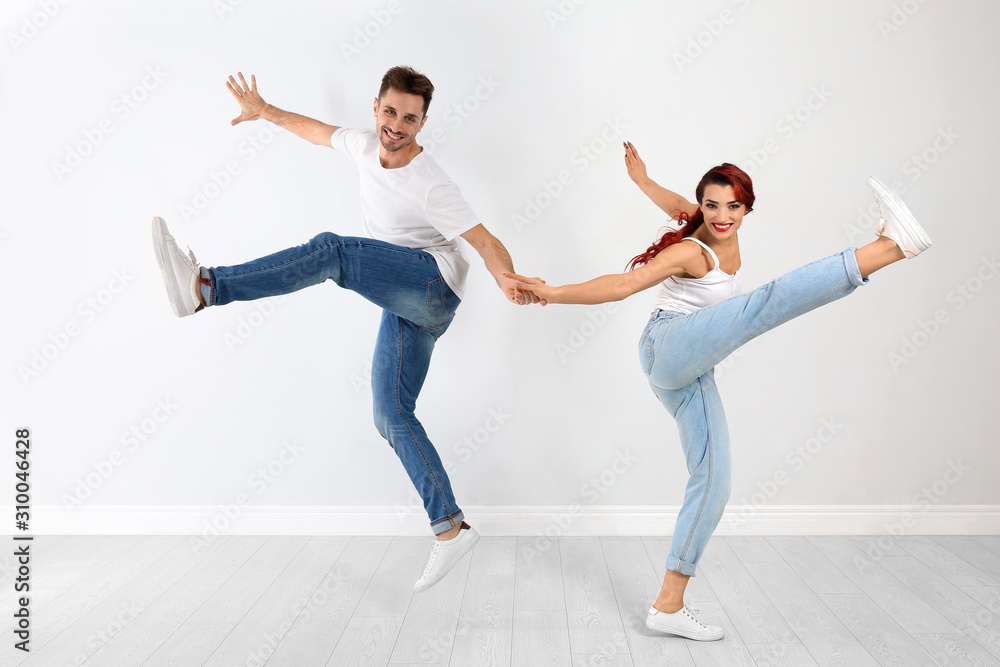 Beautiful young couple dancing near light wall Beautiful young couple dancing near light wall