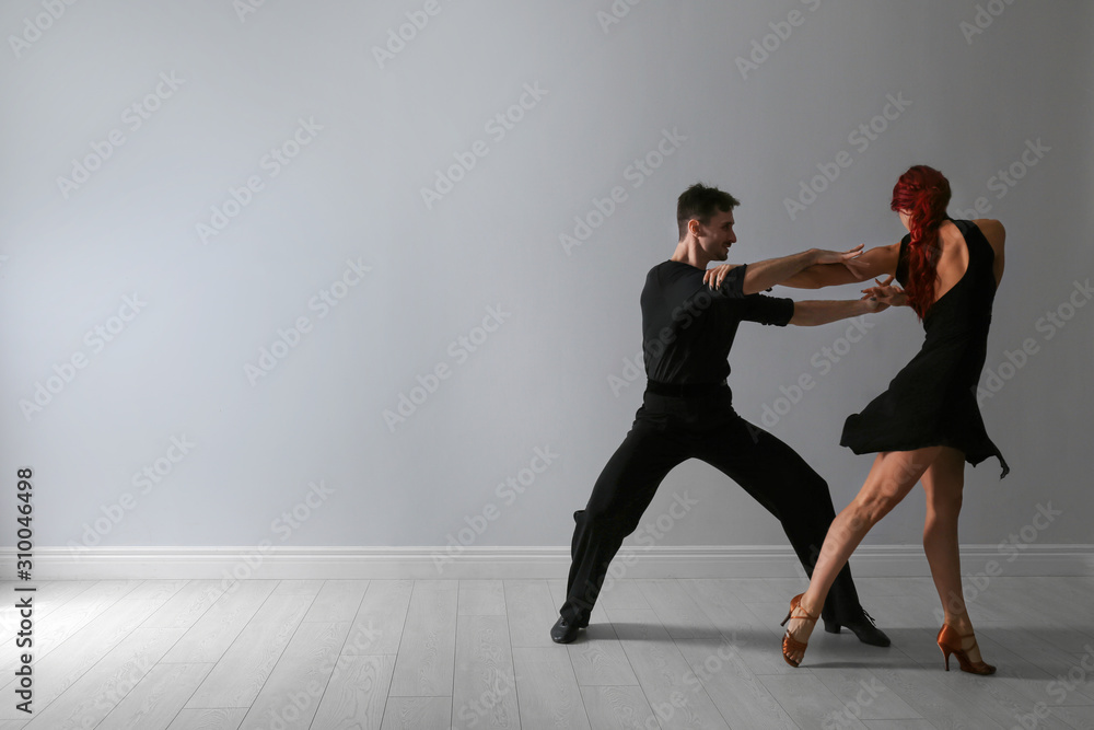Beautiful young couple dancing near light wall. Space for text Beautiful young couple dancing near light wall. Space for text