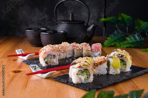 sushi roll with bacon, grilled eel, avokado red chopsticks, soy sauce, top view, sushi menu. Japanese food, on a black background and a Japanese teapot and cups.