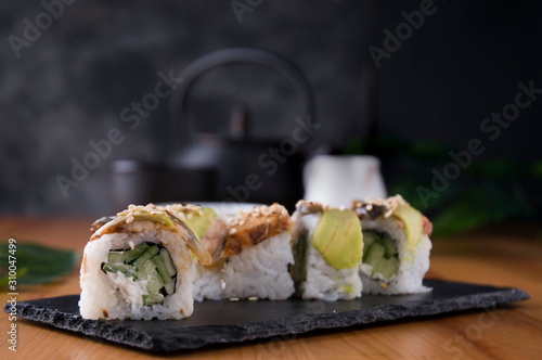 Sushi rolls with grilled eel, avocado, cucumber and cream cheese inside. Philadelphia roll with fish on a black background and a Japanese teapot and cups. Sushi menu. Japanese food.