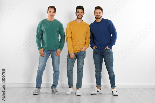 Group of young men in stylish jeans near white wall