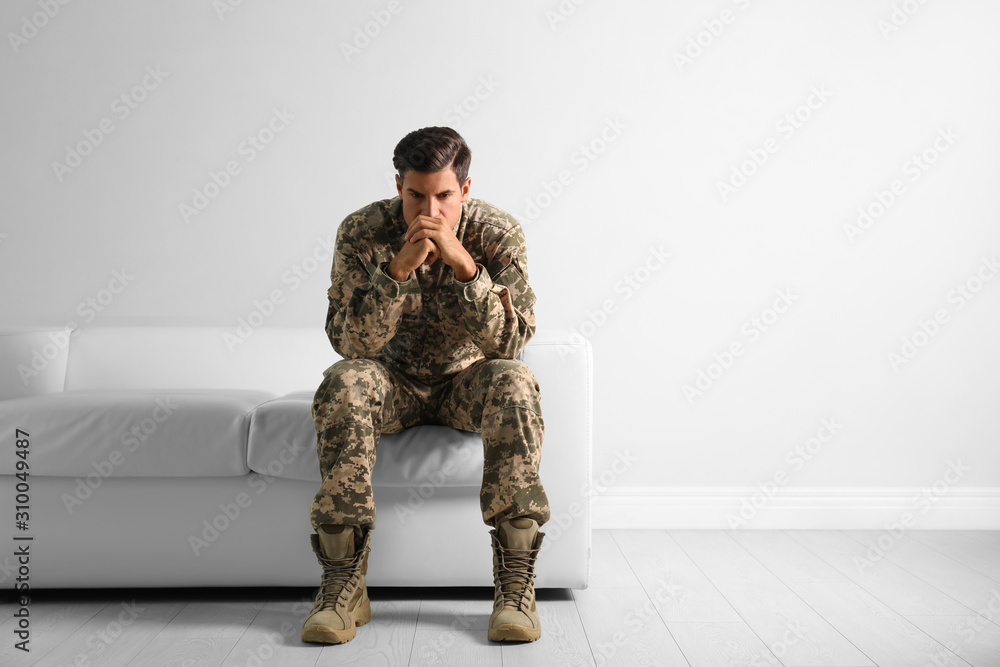 Stressed military officer sitting on sofa near white wall indoors. Space for text