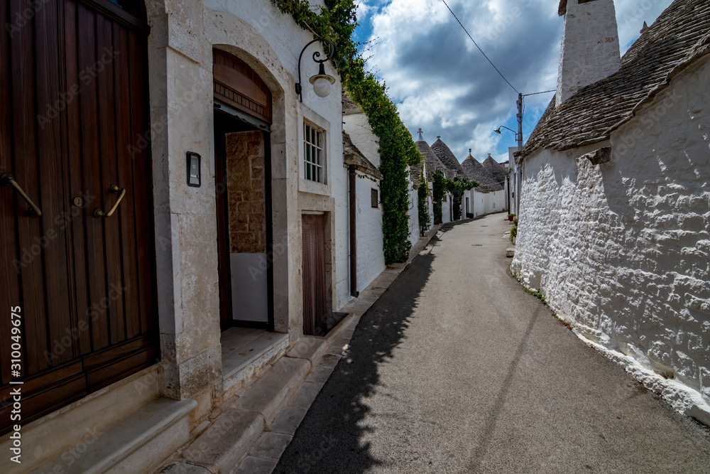 Narrow street with roofs and entrances of truli, typical whitewashed cylindrical houses in Alberobello, Puglia, Italy with amazing blue sky with clouds, street view