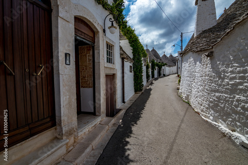 Narrow street with roofs and entrances of truli, typical whitewashed cylindrical houses in Alberobello, Puglia, Italy with amazing blue sky with clouds, street view