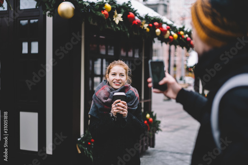 Man taking photo of redhead girlfriend with paper cup at Christmas