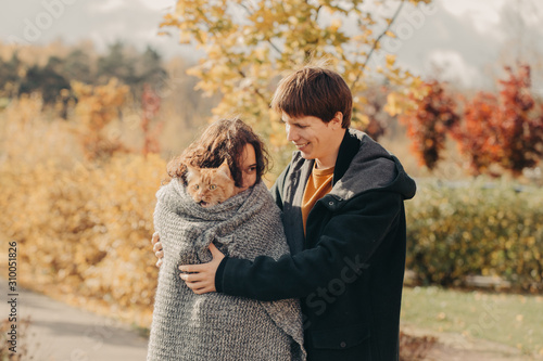 Young couple with a red cat on a background of an autumn park.