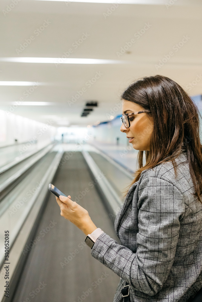 Young businesswoman using smartphone on moving walkway Young businesswoman using smartphone on moving walkway