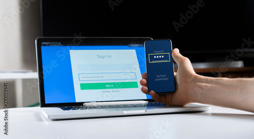 Fotografie holding a phone and working using laptop, log in on website, double-factor authe
