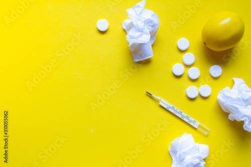 Lemon, thermometer and white medical pills on yellow background, pharmacy theme, treatment and prevention of virus. Concept of health in season of colds.