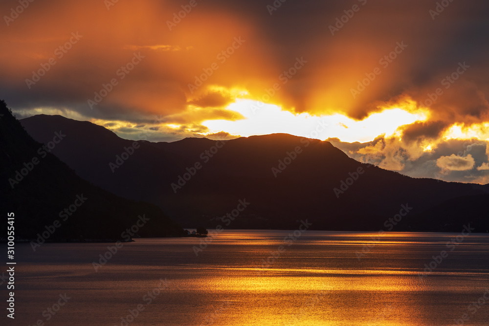 Sonnenuntergang im Storfjord in Sunnmøre, Norwegen. Sonnenstrahlen brechen duch die Wolken und spiegeln sich im Wasser.