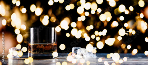 Glass of whiskey on the rocks with some ice on the table. Concept of hard liquor. Horizontal, wide screen banner format, isolated on black with festive holiday bokeh