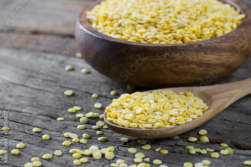 Uncooked raw yellow lentil in wooden spoon and bowl on wooden rustic table, heap of legume lentil background (Lens culinaris)