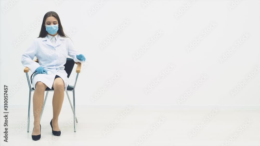 Tired therapist sitting down into the chair, taking off the medical mask, massaging her temple, stethoscope on her knees. She is sighing heavily. Tired therapist sitting down into the chair, taking off the medical mask, massaging her temple, stethoscope on her knees. She is sighing heavily.