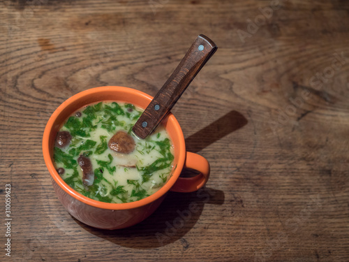 Homemade Czech traditional delicious soup Kulajda with mushroom, eggs and fresh dill in orange cup and spoon close-up on the wooden rustic table. horizontal copy space. photo