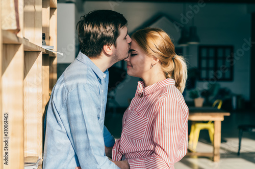 Young man kissing woman embracing standing at home
