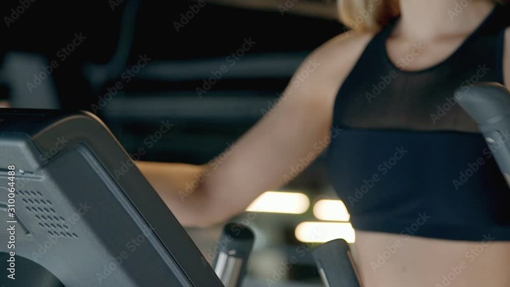 strong slim woman working out on elliptical trainer equipment in gym closeup. yound female exercising. concept of cardio, effort, sportive, shape, fitness, millenial, hispter strong slim woman working out on elliptical trainer equipment in gym closeup. yound female exercising. concept of cardio, effort, sportive, shape, fitness, millenial, hispter