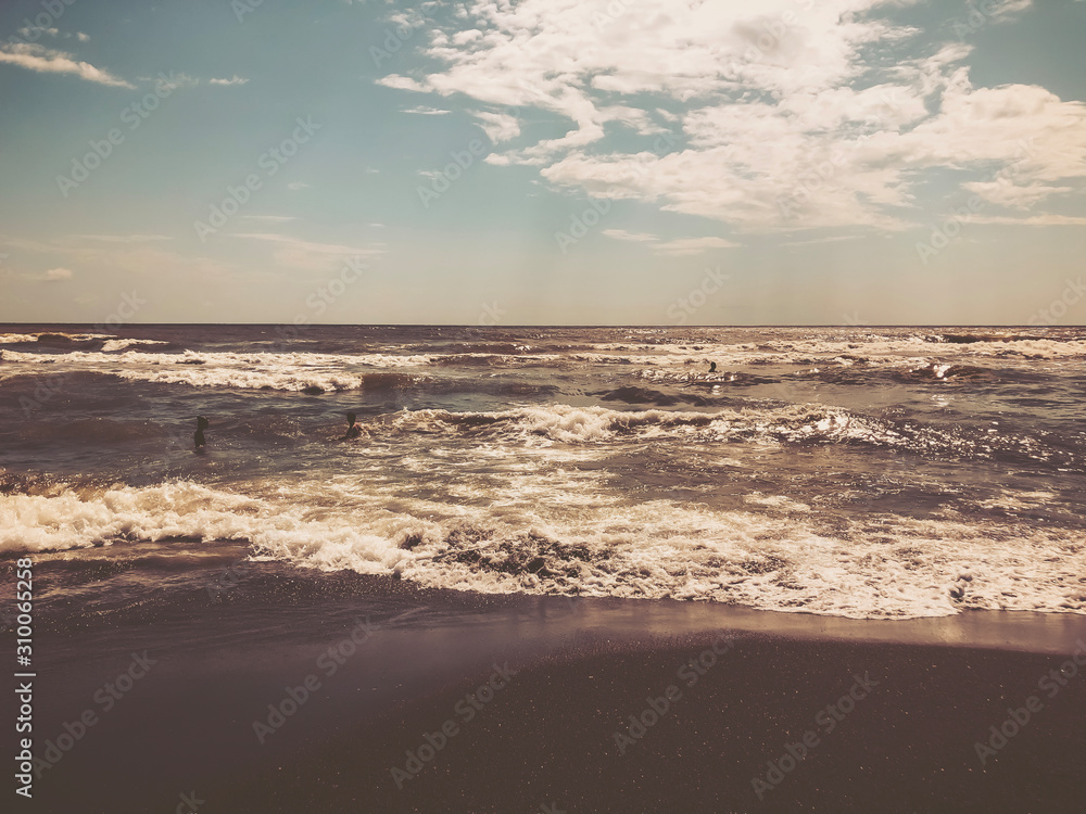 View of the sea during sunset. People swim in the sea. Glitter waves on a sandy beach. Summer sunny day, water background