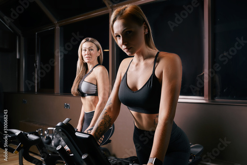 Two attractive sporty women riding exercise bikes during cycling training in gym