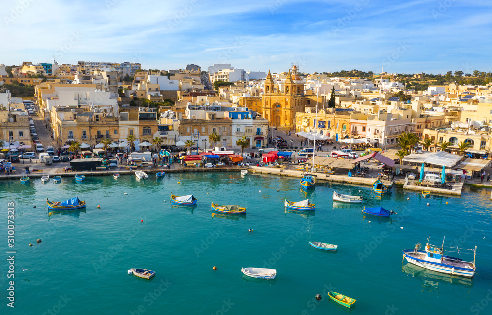 Landscape aerial view of fishing village Marsaxlokk. Traditional maltese boats on the sea, main church, coastline, blue sly. Malta
