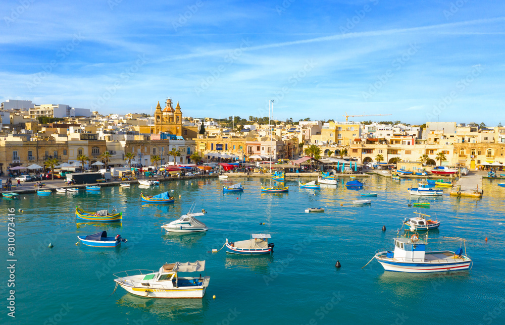 Landscape view of fishing village Marsaxlokk. Traditional maltese boats on the sea, main church, coastline, blue sly. Malta island