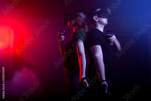 couple in modern glasses of virtual reality play a shooter against a dark neon background, a team of gamers in a game with weapons