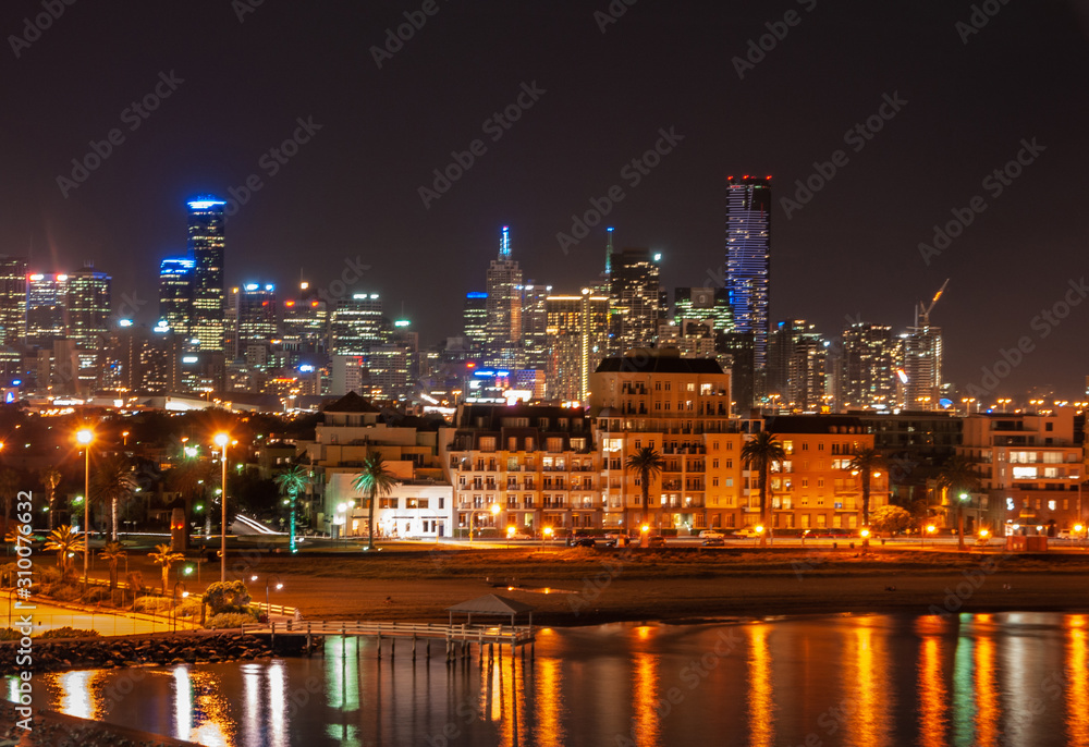 Melbourne, Australia - December 18, 2009: Port Melbourne beach area and Phillip bay at night offers light show with skyscrapers such as Eureka Tower and more in back under pick black sky. 