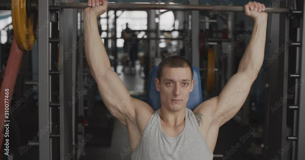 Young male athlete sit in a training room in front of the barbell, getting ready for bench press. The concept of the gym. Young male athlete sit in a training room in front of the barbell, getting ready for bench press. The concept of the gym.