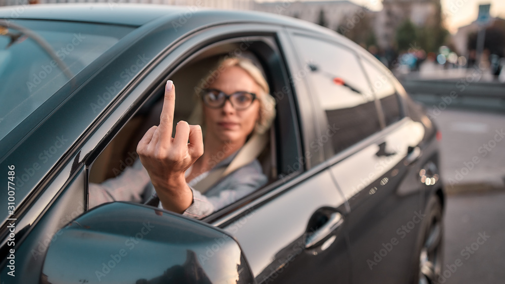 Angry businesswoman. Portrait of aggressive woman in classic wear showing middle finger to somebody while driving a ca