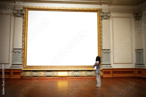 Woman with folded arms standing in front of and looking at big blank painting canvas with huge frame with negative area for your art and text.